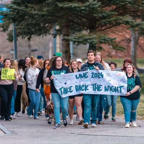 A group of students marches on campus holding a sign that reads "49ͼ2024 Take Back the Night"